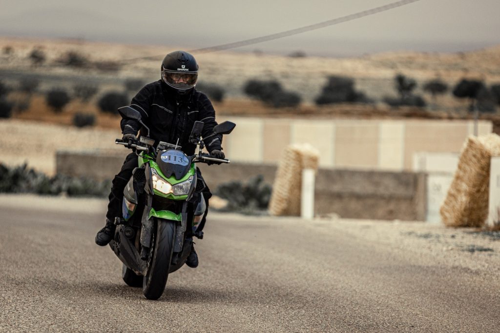 Un pilote de rallye sur sa Kawasaki Z1000 noire et verte, habillé en noir de la tête aux pieds, incluant son casque, gants et bottes, défie les routes lors d'un rallye