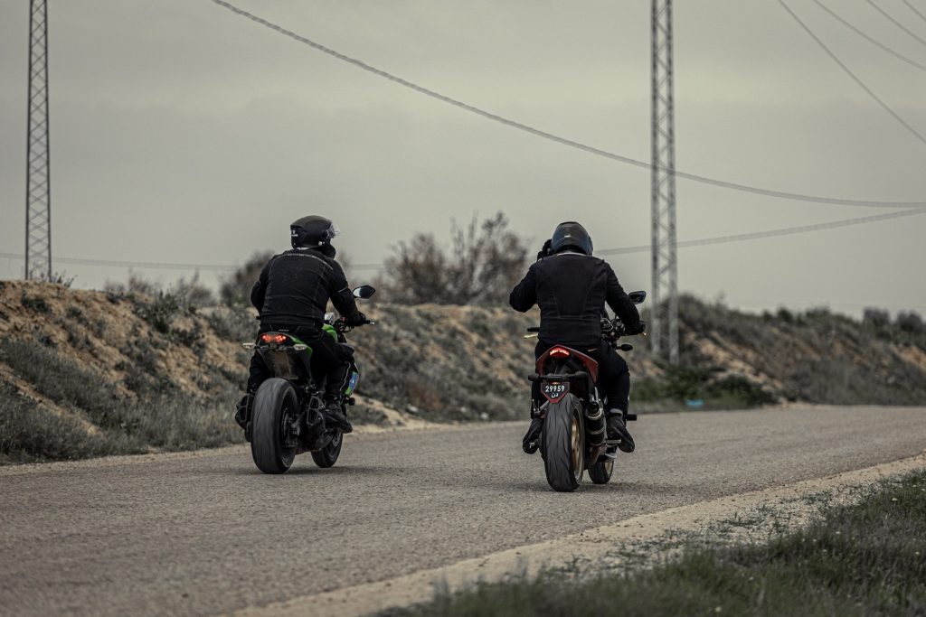 Deux pilotes de rallye sur leurs motos respectives, une Kawasaki Z1000 verte et noire et une Honda CB1000R rouge et noire , tous deux vêtus de noir, ils parcourent la route ensemble