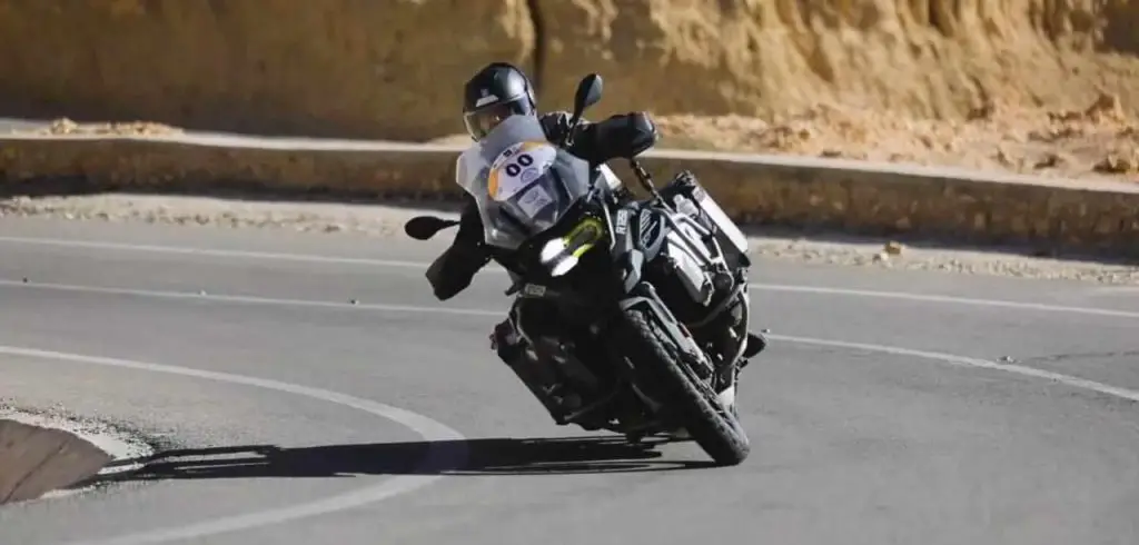 Un pilote de rallye sur sa BMW R1250 GS noire, vêtu entièrement en noir, sur la route lors d'une course de rallye, démontrant puissance et élégance